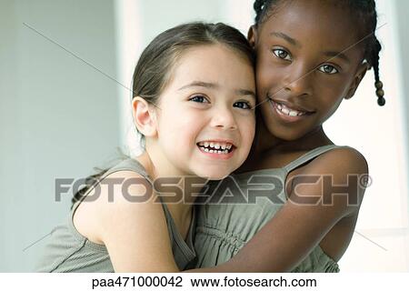 Two young female friends embracing, both smiling at camera View Large Photo Image Stock Image - Two young female friends embracing, both smiling at camera. Fotosearch
