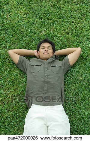 Man lying on back in grass with hands under head, eyes closed View Large Photo Image Stock Photograph - Man lying on back in grass with hands under head, eyes closed. Fotosearch