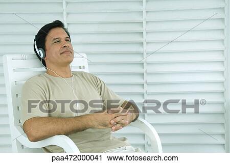 Man sitting in chair listening to headphones, eyes half-opened View Large Photo Image Stock Image - Man sitting in chair listening to headphones, eyes half-opened. Fotosearch