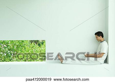 Man sitting on ledge using cell phone View Large Photo Image Stock Photo - Man sitting on ledge using cell phone. Fotosearch