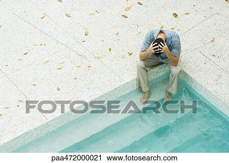 Man sitting with feet in pool, holding head, high angle view View Large Photo Image Stock Image - Man sitting with feet in pool, holding head, high angle view. Fotosearch