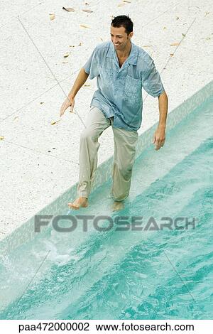 Stock Image - Man splashing in pool, fully clothed, high angle view. Fotosearch