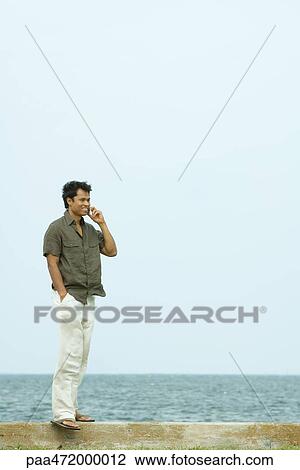 Man standing using cell phone, ocean in background View Large Photo Image Stock Image - Man standing using cell phone, ocean in background. Fotosearch