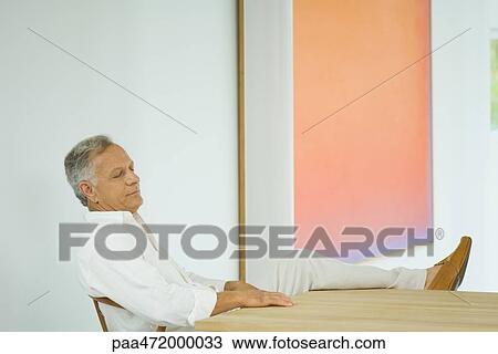 Mature man sitting at table with leg up, eyes closed View Large Photo Image Stock Image - Mature man sitting at table with leg up, eyes closed. Fotosearch