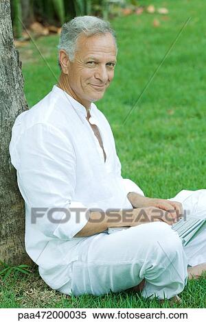 Mature man sitting outdoors using laptop computer, smiling at camera View Large Photo Image Stock Photography - Mature man sitting outdoors using laptop computer, smiling at camera. Fotosearch
