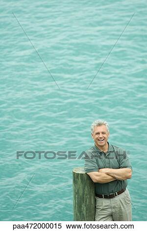Stock Photography - Mature man standing on pier with arms folded, smiling at camera. Fotosearch