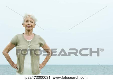 Senior woman standing with hands on hips, smiling at camera, portrait View Large Photo Image Stock Image - Senior woman standing with hands on hips, smiling at camera, portrait. Fotosearch