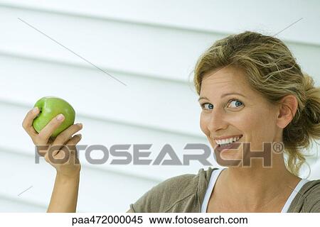 Woman holding up apple and smiling at camera View Large Photo Image Stock Photography - Woman holding up apple and smiling at camera. Fotosearch