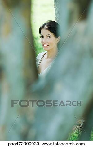Woman looking between tree branches, smiling at camera View Large Photo Image Stock Image - Woman looking between tree branches, smiling at camera. Fotosearch