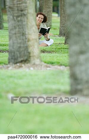 Woman sitting among trees holding book, looking away View Large Photo Image Stock Photograph - Woman sitting among trees holding book, looking away. Fotosearch