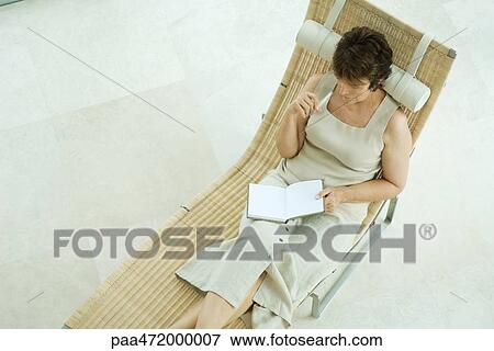 Woman sitting on lounge chair writing in diary, high angle view View Large Photo Image Stock Photo - Woman sitting on lounge chair writing in diary, high angle view. Fotosearch