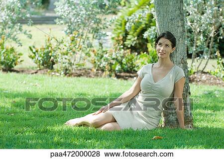 Woman sitting on the ground under tree, smiling, looking up View Large Photo Image Stock Photo - Woman sitting on the ground under tree, smiling, looking up. Fotosearch