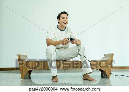 Young man playing video game, smiling View Large Photo Image Picture - Young man playing video game, smiling. Fotosearch