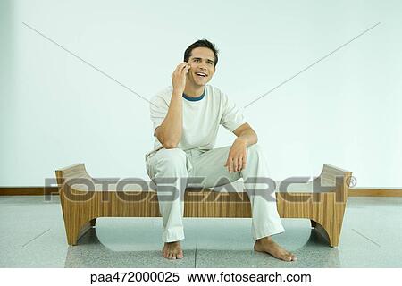 Stock Photography - Young man sitting on bench using cell phone. Fotosearch