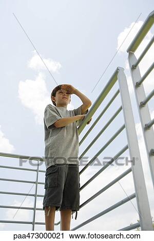 Boy standing on balcony shading eyes, looking at view View Large Photo Image Stock Image - Boy standing on balcony shading eyes, looking at view. Fotosearch