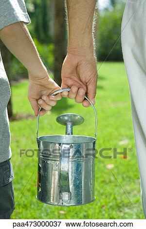 Cropped rear view of man and child carrying watering can together View Large Photo Image Stock Photo - Cropped rear view of man and child carrying watering can together. Fotosearch
