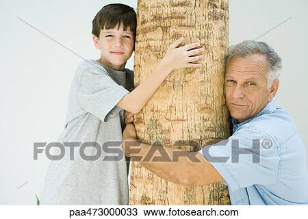 Grandfather and grandson hugging tree trunk, smiling at camera View Large Photo Image Stock Image - Grandfather and grandson hugging tree trunk, smiling at camera. Fotosearch