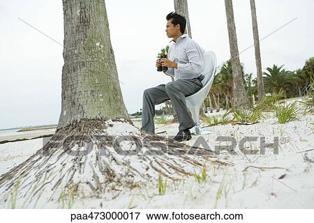 Man sitting in chair on beach looking at view, holding binoculars View Large Photo Image Stock Photo - Man sitting in chair on beach looking at view, holding binoculars. Fotosearch