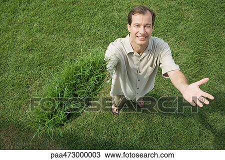 Man standing and holding clump of grass in one hand, smiling at camera, high angle view View Large Photo Image Stock Image - Man standing and holding clump of grass in one hand, smiling at camera, high angle view. Fotosearch