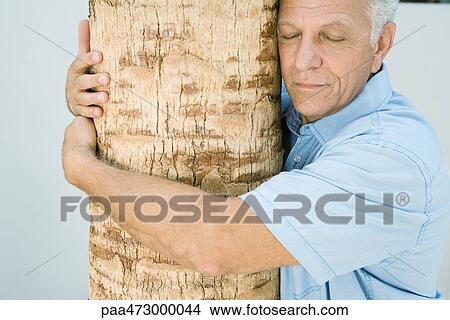 Mature man hugging tree trunk, eyes closed, smiling View Large Photo Image Picture - Mature man hugging tree trunk, eyes closed, smiling. Fotosearch