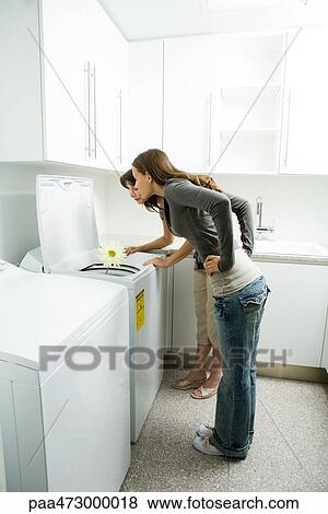 Stock Photo - Mother and daughter looking down at daisy growing out of washing machine. Fotosearch