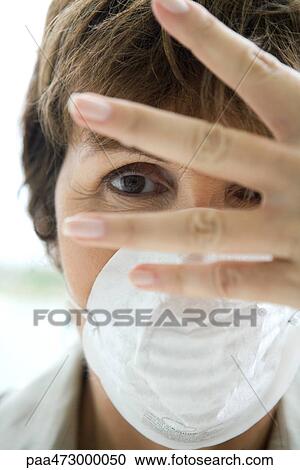 Stock Image - Woman wearing pollution mask, looking through fingers at camera. Fotosearch