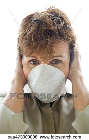 Stock Photo - Woman with hands over ears wearing pollution mask, looking at camera. Fotosearch