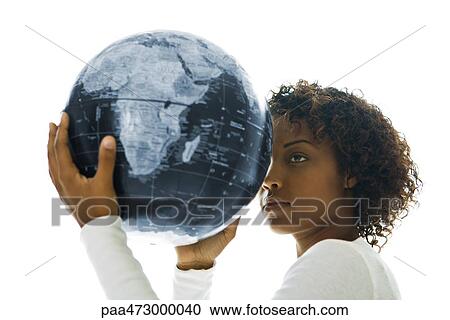 Stock Image - Young woman holding globe against forehead, side view. Fotosearch