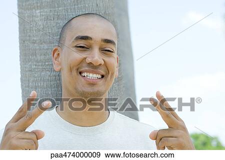 Man giving peace sign and smiling at camera, portrait View Large Photo Image Stock Photo - Man giving peace sign and smiling at camera, portrait. Fotosearch