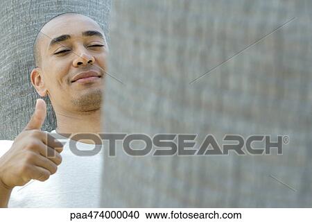 Stock Image - Man giving thumbs up, smiling at camera, eyes half-opened. Fotosearch