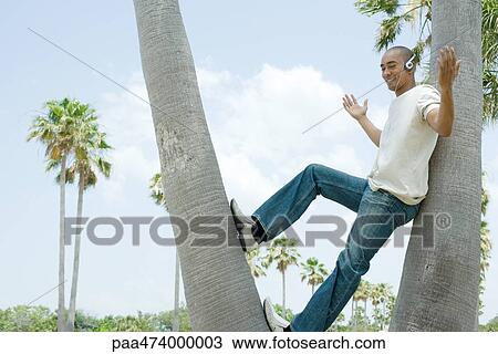 Man leaning against tree trunk listening to headphones, arms out, hands raised View Large Photo Image Stock Image - Man leaning against tree trunk listening to headphones, arms out, hands raised. Fotosearch