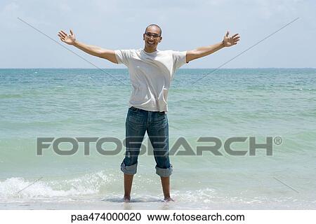 Man standing ankle deep in ocean with arms outstretched, smiling at camera View Large Photo Image Stock Image - Man standing ankle deep in ocean with arms outstretched, smiling at camera. Fotosearch