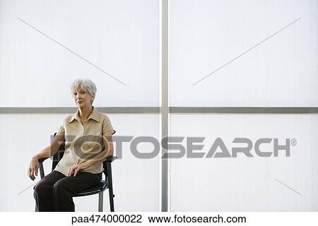Stock Image - Senior woman sitting in chair looking at camera. Fotosearch