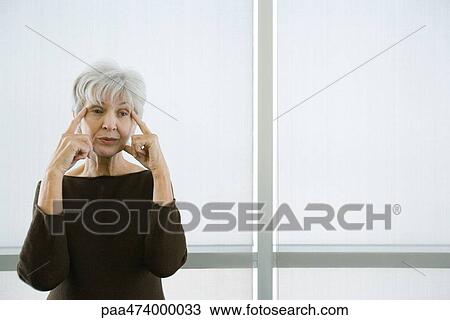 Senior woman standing with fingers on temples, looking away View Large Photo Image Stock Image - Senior woman standing with fingers on temples, looking away. Fotosearch