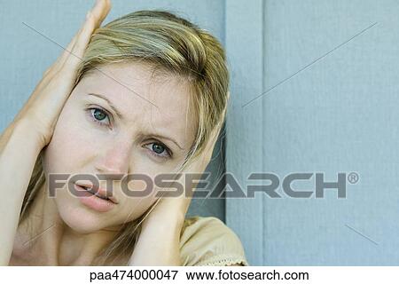 Stock Photo - Woman covering ears with hands, frowning at camera. Fotosearch