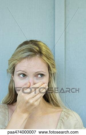 Stock Photo - Woman covering mouth with hand, looking away, close-up. Fotosearch