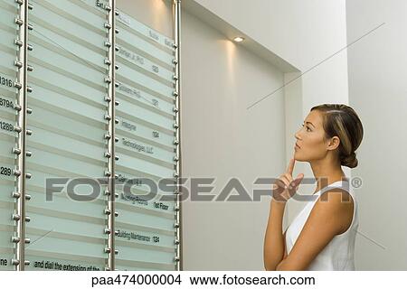Picture - Woman looking at business directory, index finger on chin. Fotosearch