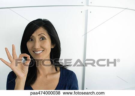 Stock Photo - Woman making OK hand gesture, smiling at camera. Fotosearch