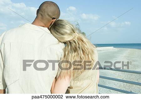 Couple standing arm in arm looking at view, woman's head on man's shoulder, rear view View Large Photo Image Stock Image - Couple standing arm in arm looking at view, woman's head on man's shoulder, rear view. Fotosearch