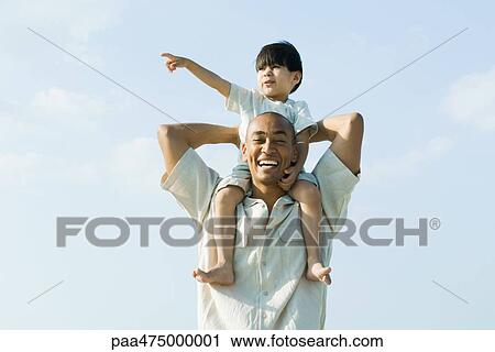 Father carrying son on shoulders and smiling at camera, child pointing and looking away View Large Photo Image Stock Image - Father carrying son on shoulders and smiling at camera, child pointing and looking away. Fotosearch