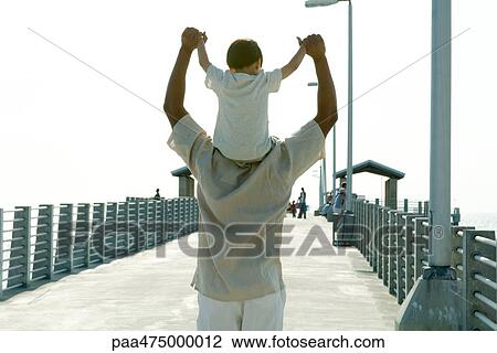Father carrying son on shoulders, holding hands, rear view View Large Photo Image Stock Image - Father carrying son on shoulders, holding hands, rear view. Fotosearch