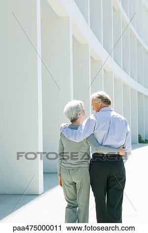 Mature couple walking with arms around each other, rear view View Large Photo Image Stock Image - Mature couple walking with arms around each other, rear view. Fotosearch