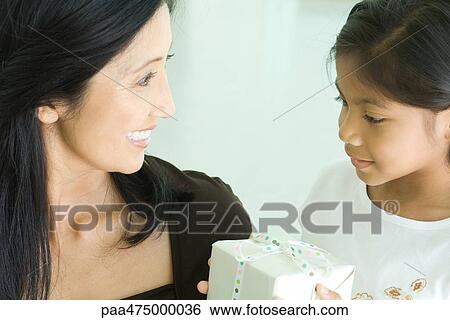 Stock Photograph - Mother and daughter smiling together, girl holding gift. Fotosearch