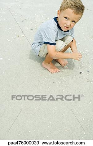 Boy crouching in sand, looking up at camera View Large Photo Image Stock Photo - Boy crouching in sand, looking up at camera. Fotosearch