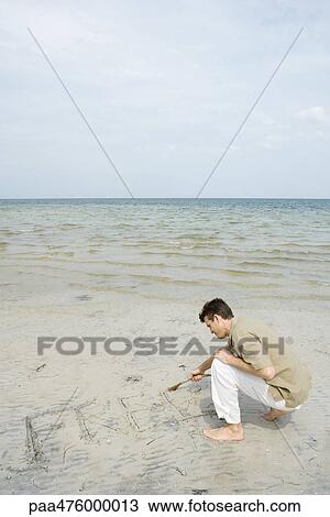 Man crouching on beach writing the word "free" in sand with a stick View Large Photo Image Stock Image - Man crouching on beach writing the word "free" in sand with a stick. Fotosearch