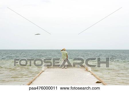 Man standing on pier looking at ocean, rear view View Large Photo Image Stock Image - Man standing on pier looking at ocean, rear view. Fotosearch