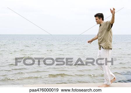 Man walking barefoot with arms out along water's edge View Large Photo Image Stock Photo - Man walking barefoot with arms out along water's edge. Fotosearch