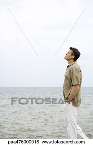 Man walking beside ocean with hands in pockets, looking up View Large Photo Image Stock Photograph - Man walking beside ocean with hands in pockets, looking up. Fotosearch