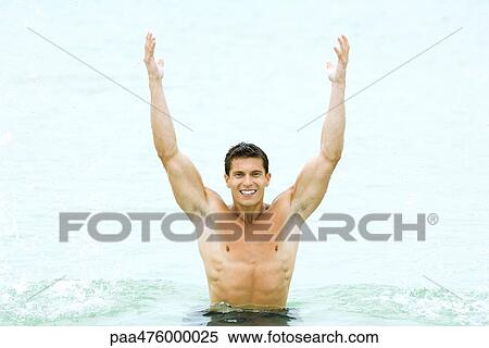 Stock Photography - Muscular man standing in swimming pool with arms raised, smiling at camera. Fotosearch