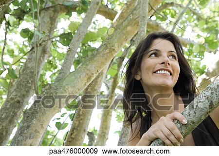 Stock Photo - Woman leaning against tree and smiling, low angle view. Fotosearch